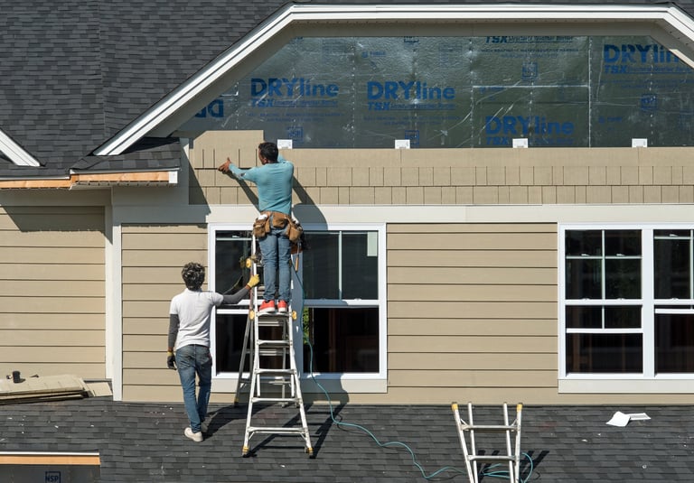 Construction workers install shake siding on second story Gambrel roofline as part of new condo housing development.