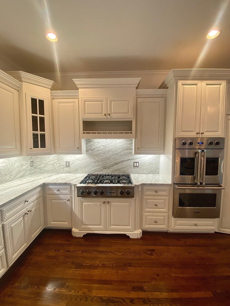 Modern luxury kitchen with cream cabinetry, marble backsplash, stainless steel appliances, and hardwood flooring