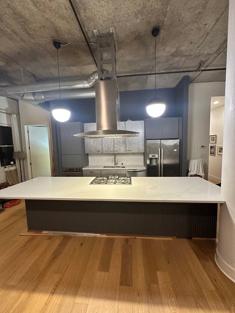 Modern industrial kitchen with white countertop island, stainless steel range hood, concrete ceiling, and hardwood flooring